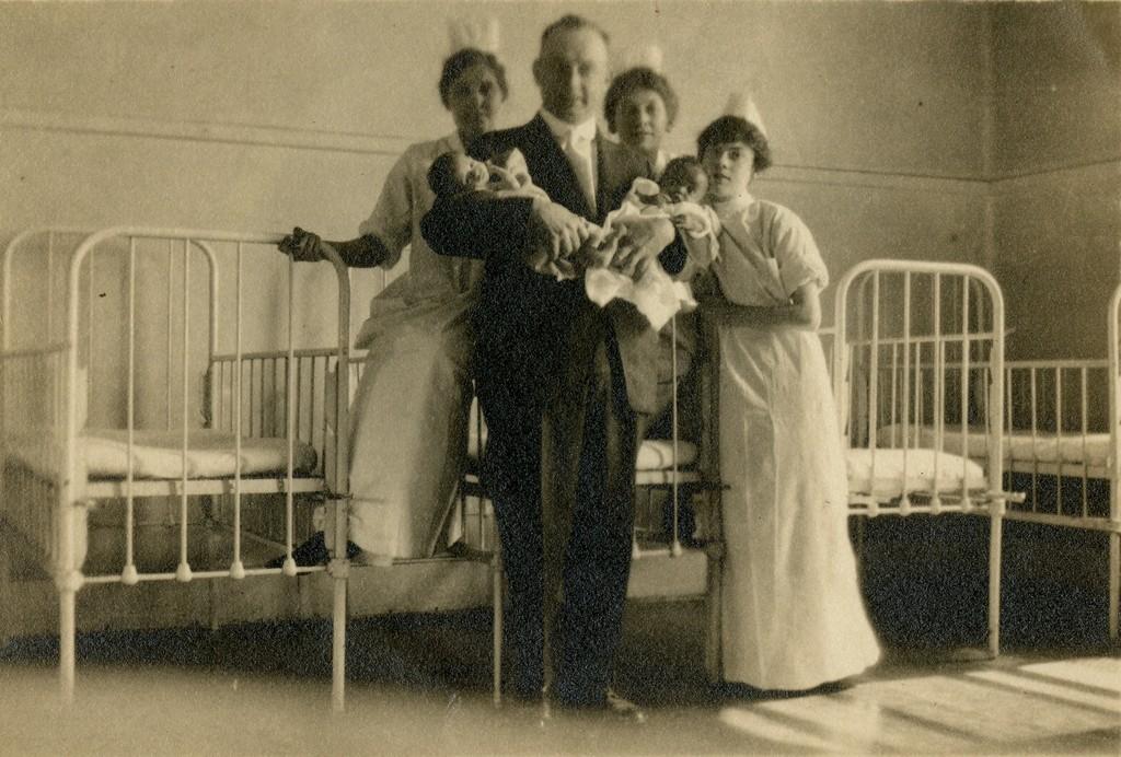 Three student nurse pose with a physician holding two infants, prior to 1904