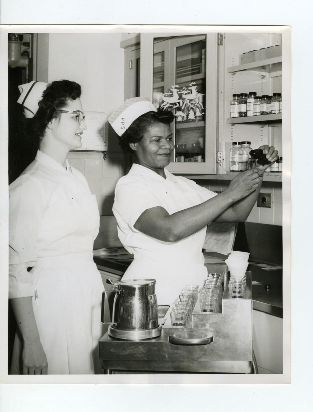 An instructor shows a practical nurse student how to pour medication, c. 1958