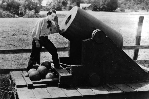Buster Keaton putting his ear to cannon in a scene from the film 'The General', 1926