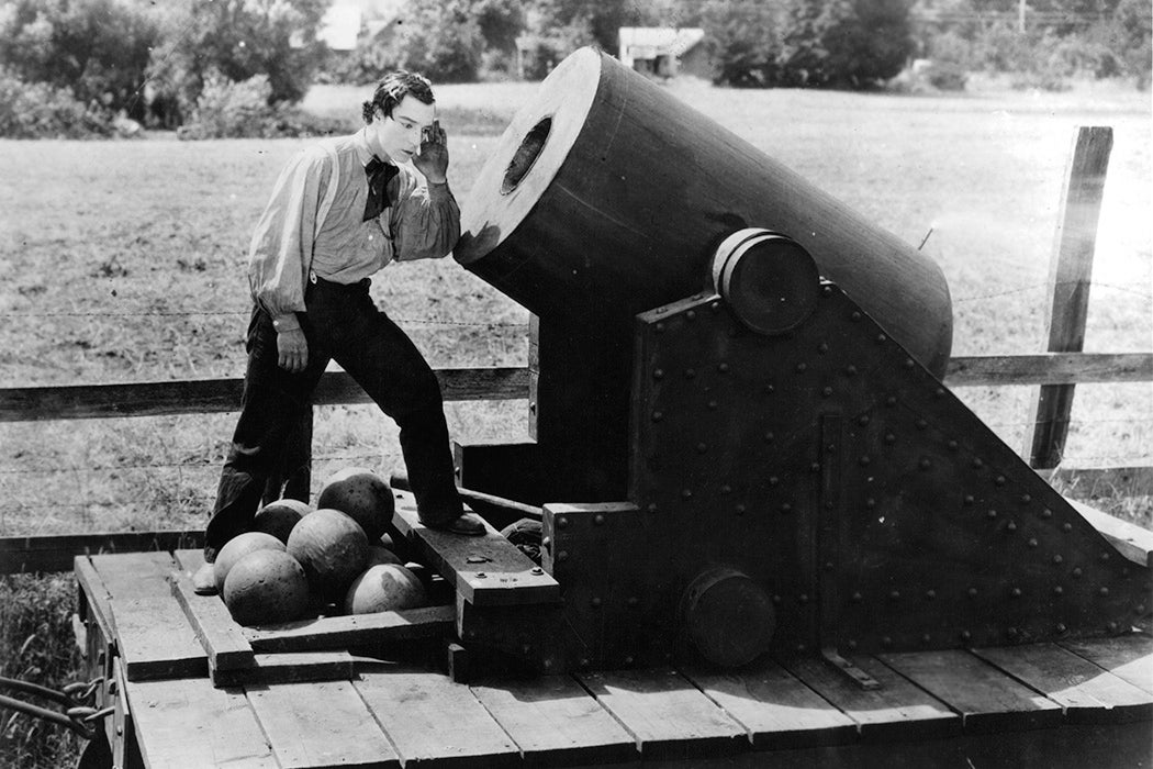 Buster Keaton putting his ear to cannon in a scene from the film 'The General', 1926