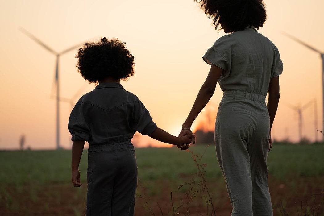A parent and child near windmills at sunset