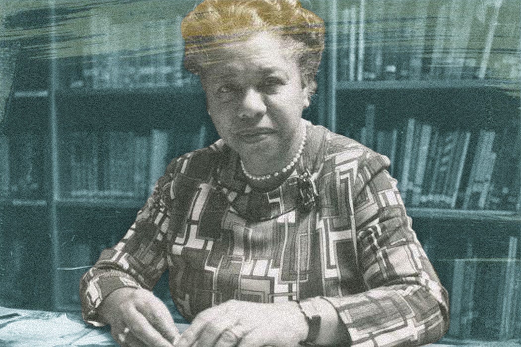 Black and white photograph of Augusta Baker seated at a desk with papers spread out before her.