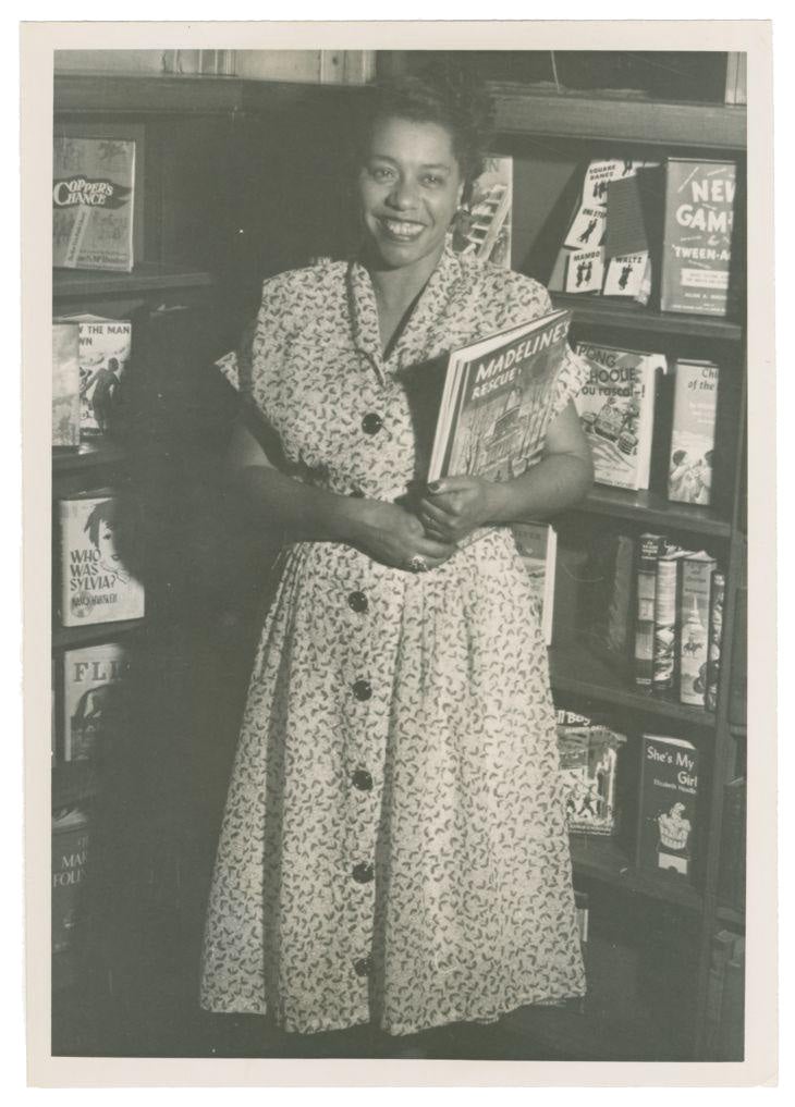 Photograph of Augusta Baker holding Madeline's Rescue and smiling at camera.