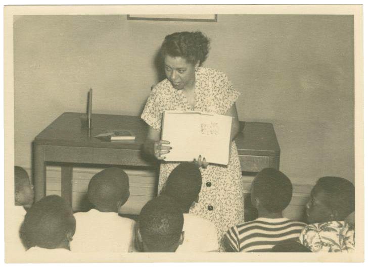 Photograph of Augusta Baker reading a story to a group of children.